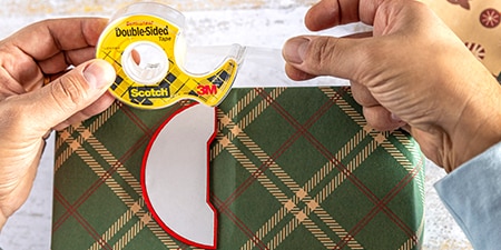 Fixation de décorations sur un cadeau emballé en utilisant le ruban adhésif double face Scotch®

