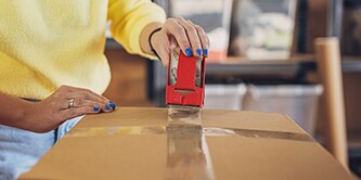 Femme fermant un carton avec du ruban d’emballage Scotch®.
