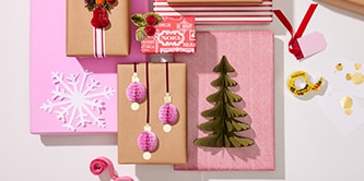 Décorations de Noël et loisirs créatifs en papier comme des arbres et des boules attachés à des cadeaux emballés en utilisant le ruban adhésif double face Scotch®
